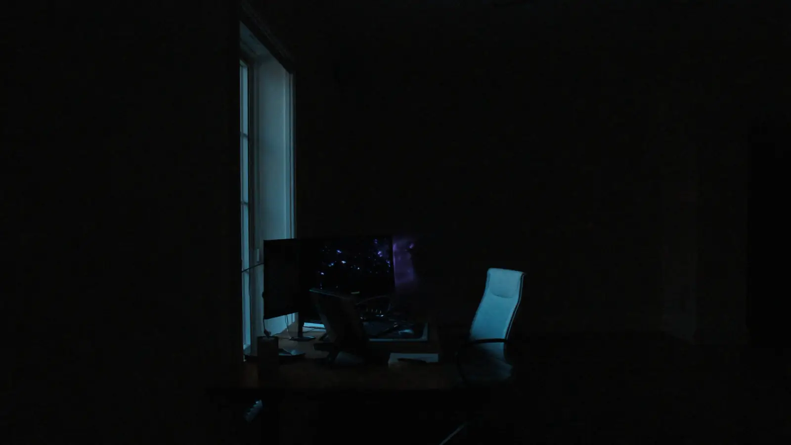 An empty desk before dawn, monitors switched off, chair pushed back