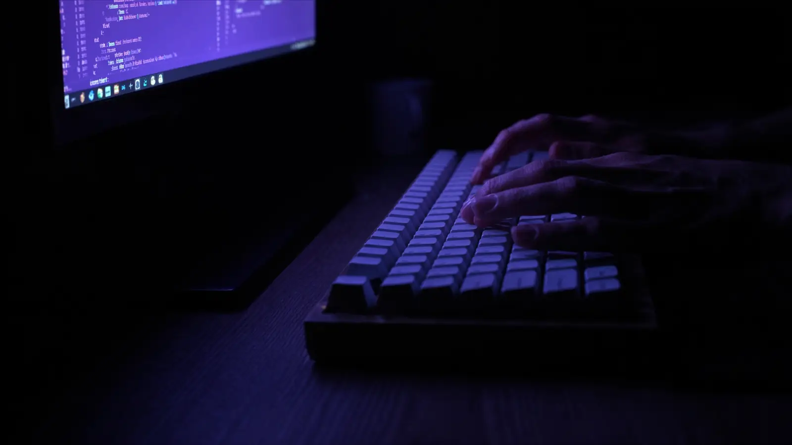 Close detail of hands on a mechanical keyboard lit by code on a monitor